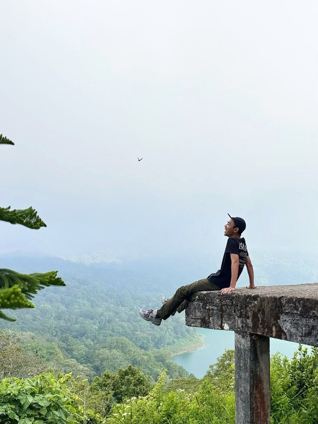Batuh sitting on a viewpoint ledge above a Bali valley